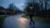 Løber set bagfra med en vest med rødt lysende LED-lys og grønne refleksbånd på en mørk villavej